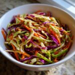 A close-up of a vibrant cabbage salad mix featuring shredded green cabbage, red cabbage, and carrots, tossed in a light dressing.