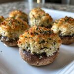 Close-up of baked stuffed mushrooms with a golden, crispy breadcrumb topping and fresh parsley garnish.