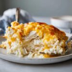 A close-up serving of creamy, cheesy chicken and rice casserole topped with melted cheddar cheese.