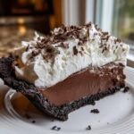 A rich slice of Christmas chocolate cream pie featuring a dark crust, thick chocolate filling, and whipped cream topped with shavings.