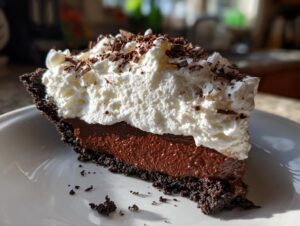A decadent slice of Christmas chocolate cream pie featuring a dark crust, rich chocolate filling, and thick whipped cream topping with shavings.