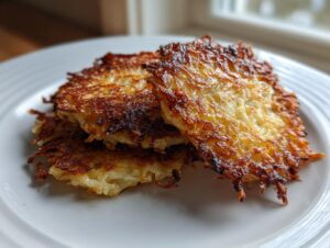 Close-up of three golden-brown, crispy potato latkes stacked on a white plate, ready to eat.
