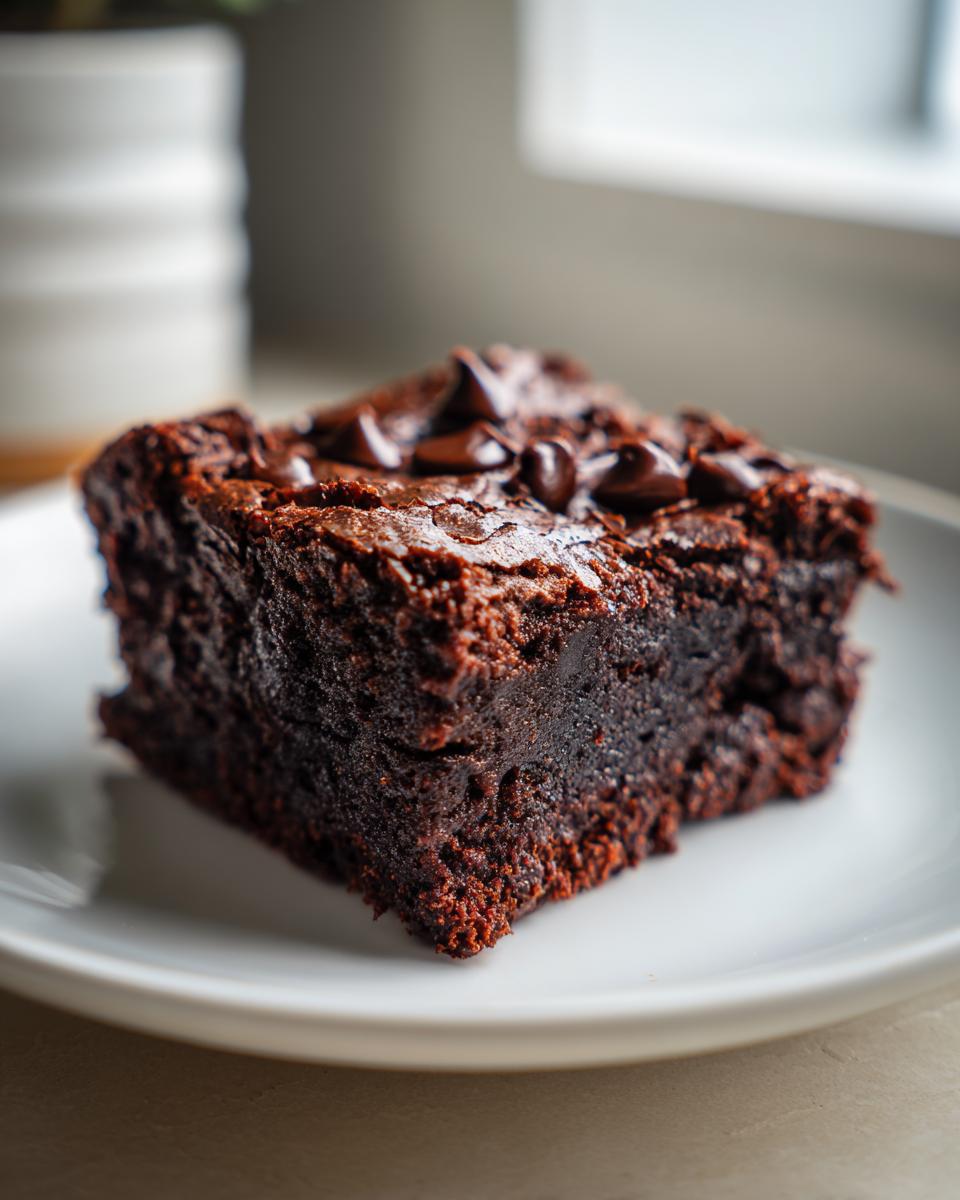 A close-up of a fudgy square of Sweet potato brownies topped with melted chocolate chips on a white plate.