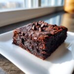 A single, rich, dark square of fudgy sweet potato brownies topped with chocolate chips, resting on a white plate.