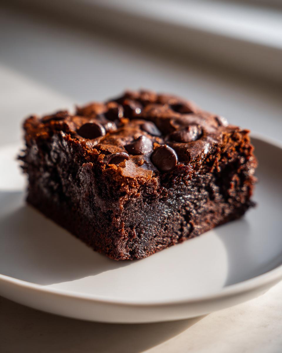 A single, fudgy square of sweet potato brownies topped with melted chocolate chips, sitting on a light plate.