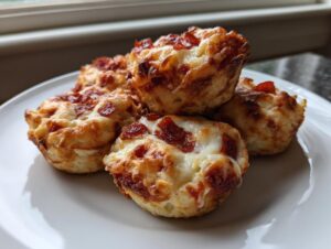 A close-up of several golden brown pizza muffins topped with melted cheese and pepperoni slices on a white plate.
