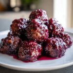 A pile of glistening Grape Jelly Meatballs coated in a rich, dark purple glaze served on a white plate.
