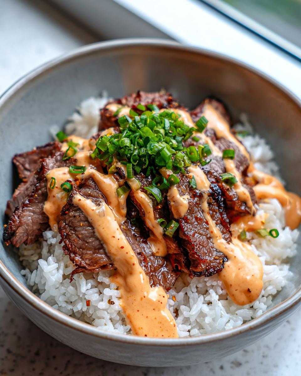 A close-up of Korean BBQ steak rice bowls featuring sliced marinated steak over white rice, drizzled with spicy mayo and topped with green onions.