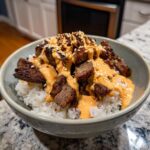 Close-up of Korean BBQ steak rice bowls topped with creamy sauce and sesame seeds.