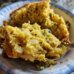 Close-up of a spoonful of moist cornbread dressing with visible onions and green peppers.