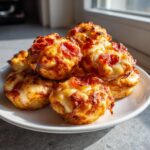 A stack of freshly baked, cheesy pepperoni pizza muffins piled high on a white plate.