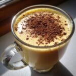 Close-up of a glass mug filled with rich, creamy eggnog, topped with grated chocolate.