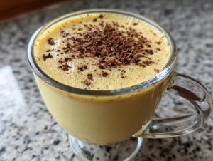 Close-up of a glass mug filled with rich, creamy eggnog, topped with dark chocolate shavings.