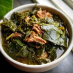 Close-up of a bowl filled with silky collard greens cooked with tender shredded meat in rich broth.
