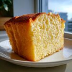 A close-up, brightly lit slice of moist vanilla cake showing its soft, airy crumb texture on a white plate.