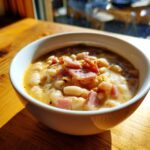 A close-up of a creamy bowl of white bean and ham soup topped with diced ham and pepper.