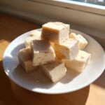 A stack of creamy, pale white chocolate fudge cubes piled high on a white plate.