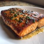 Close-up of a glistening, perfectly cooked piece of air fryer salmon topped with butter sauce and fresh parsley.