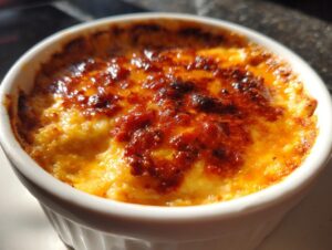Close-up of a baked chili cheese dip in a white ramekin, showing a bubbly, browned, and cheesy top layer.
