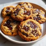 A stack of freshly baked, chewy chocolate chip cookie rounds topped with flaky sea salt.