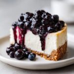 A close-up of a creamy slice of blueberry cheesecake topped with rich blueberry sauce and fresh berries.