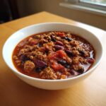Close-up of a white bowl filled with rich, meaty high protein chili featuring kidney beans and black beans.