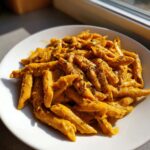 A close-up of penne pasta coated in a vibrant orange butternut squash pasta sauce, topped with herbs.