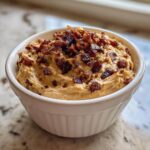 Creamy caramelized onion dip topped generously with crispy bacon bits, served in a white ramekin.
