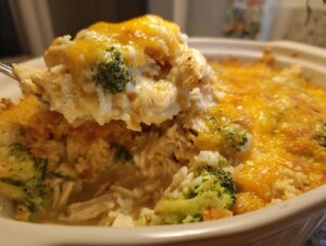 A spoonful of creamy chicken broccoli rice casserole topped with melted cheddar cheese being lifted from the baking dish.