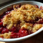 Close-up of a baked cherry dump cake showing juicy red cherries under a golden, crumbly topping.