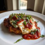 A close-up of a golden-brown, breaded chicken parmesan recipe topped with melted mozzarella, rich marinara sauce, and fresh basil.