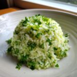 A perfectly molded serving of bright cilantro lime rice topped with chopped fresh cilantro on a white plate.