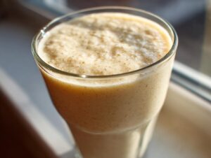 Close-up of a thick, creamy banana smoothie in a clear glass, illuminated by sunlight.