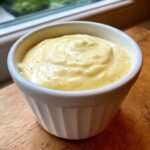 Close-up of thick, yellow homemade garlic aioli served in a small white fluted ramekin.