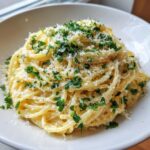 Close-up of a bowl of creamy garlic parmesan pasta generously topped with grated cheese and fresh chopped parsley.