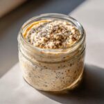 Close-up of creamy overnight oats in a glass jar, topped generously with chia seeds, ready to eat.