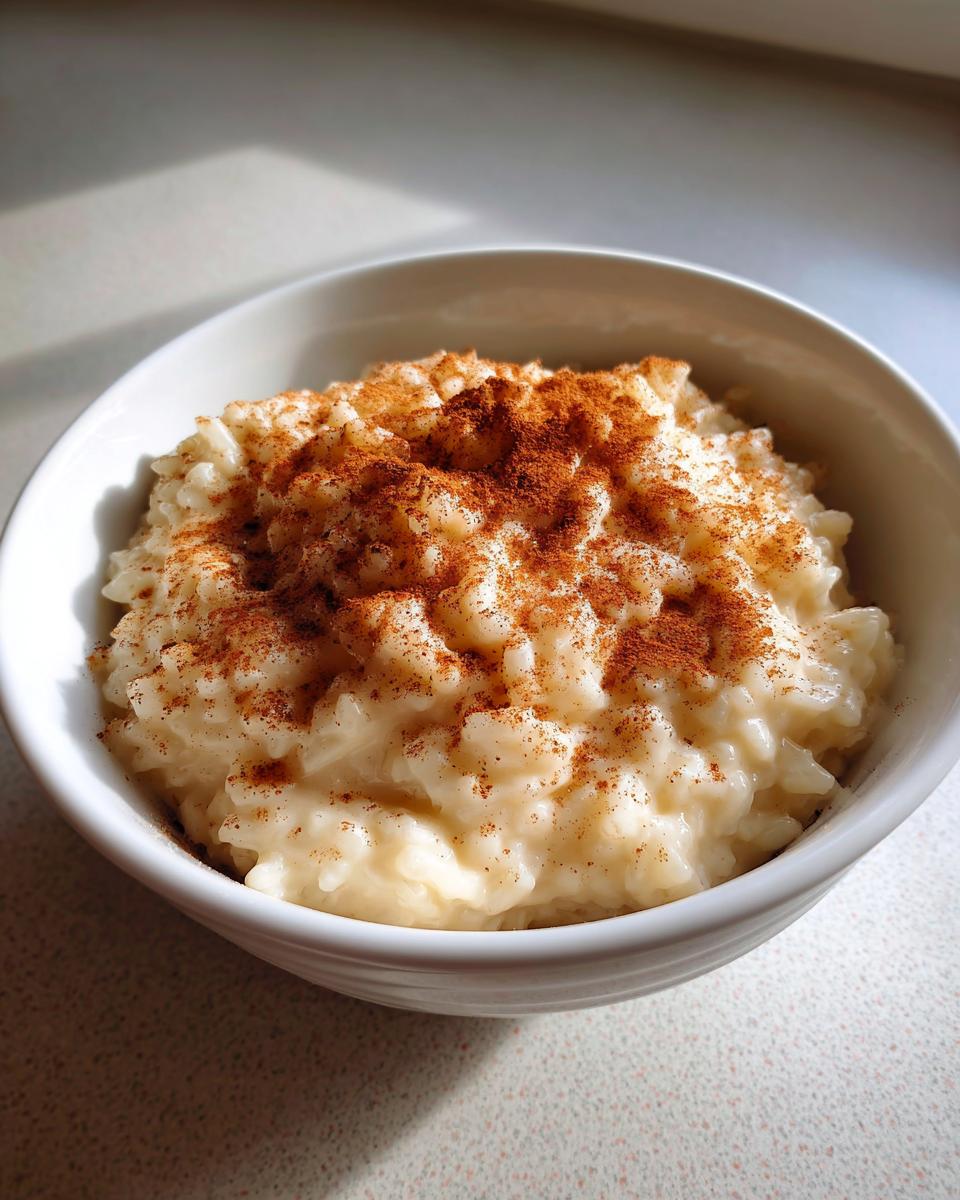 A close-up of creamy rice pudding served in a white bowl and generously dusted with cinnamon.