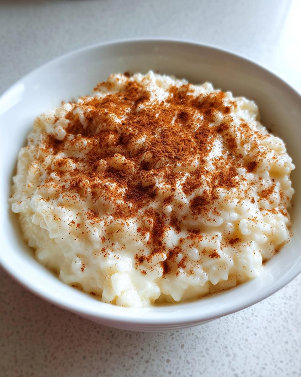 Close-up of a white bowl filled with creamy rice pudding generously dusted with ground cinnamon.