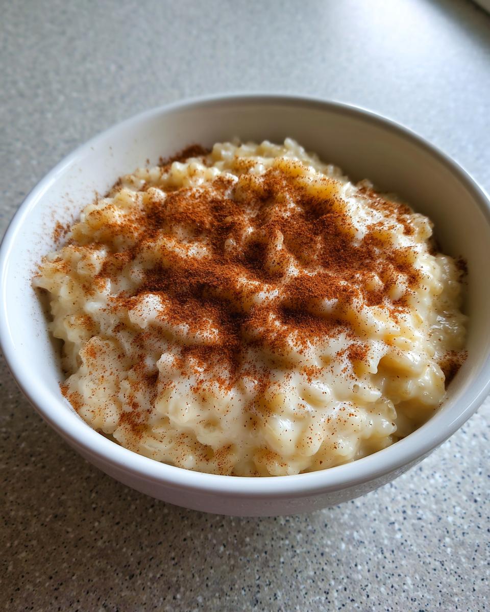 Close-up of a white bowl filled with creamy rice pudding generously dusted with ground cinnamon.
