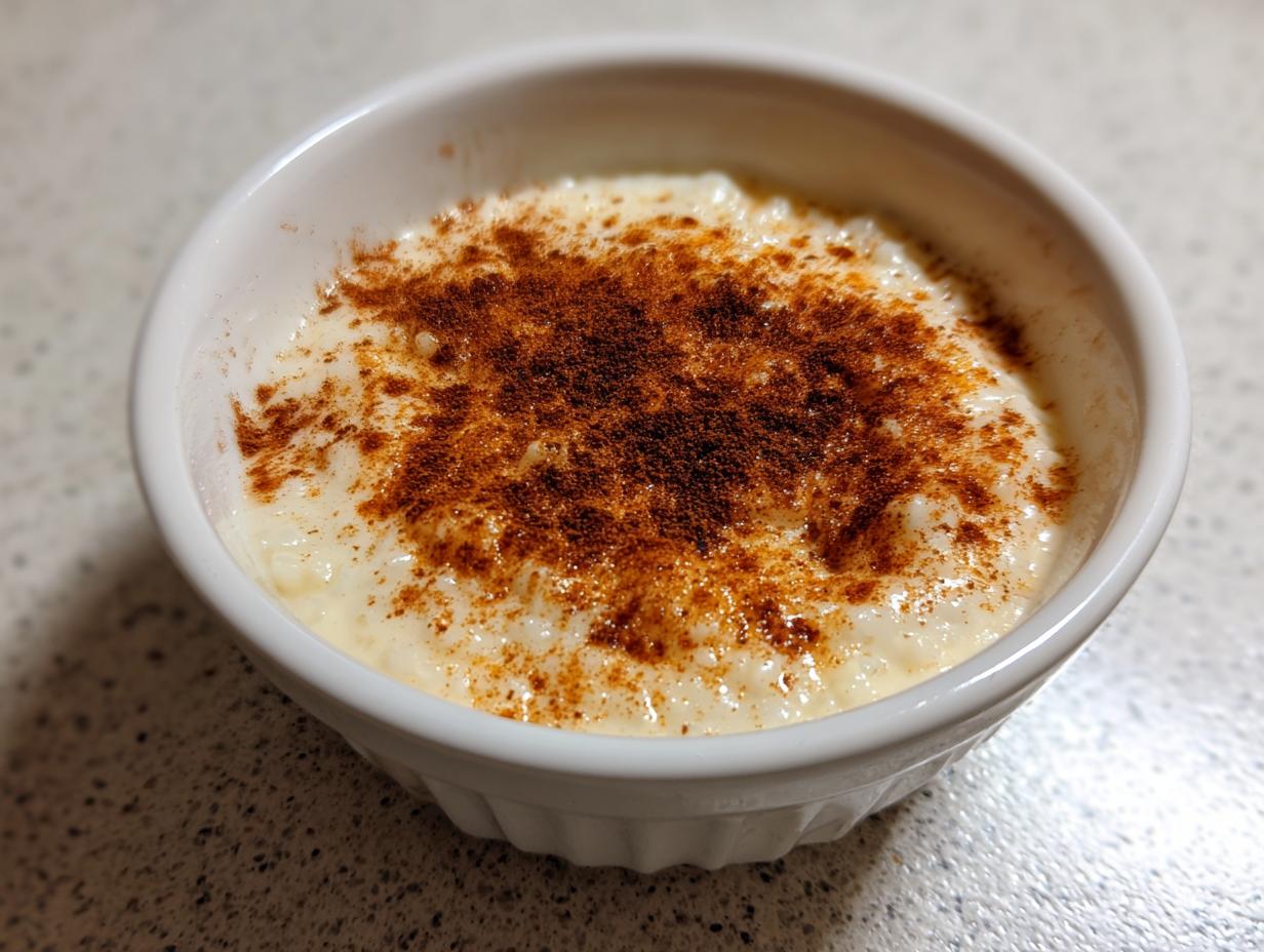 A close-up of creamy rice pudding topped generously with ground cinnamon served in a small white bowl.