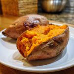 Close-up of a perfectly baked sweet potatoes, one split open revealing the bright orange, fluffy interior.