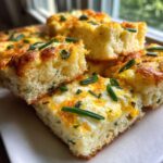 Close-up of fluffy, square slices of sheet pan eggs baked with melted cheese and topped with fresh green chives.