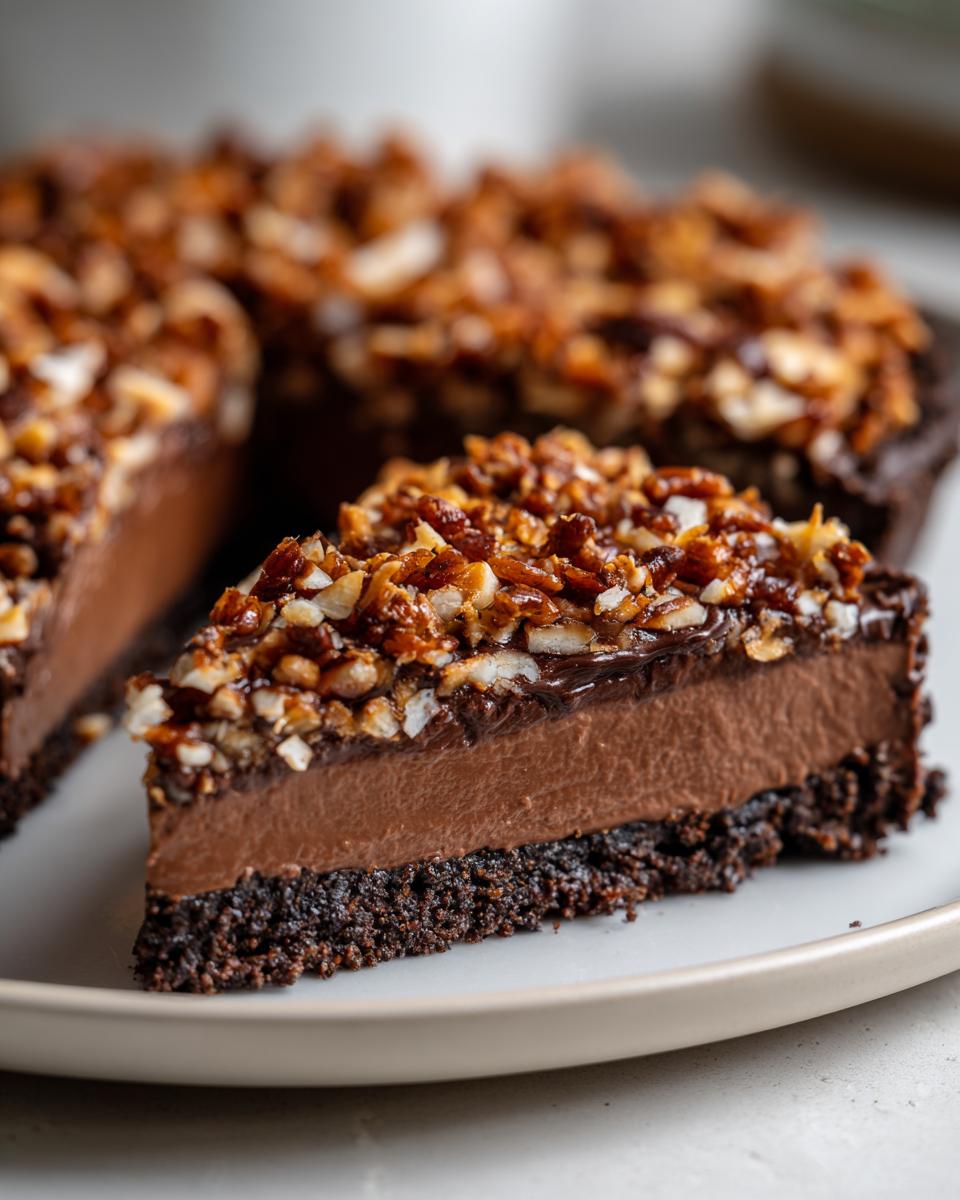Close-up of a slice of german chocolate pie showing a dark crust, thick chocolate filling, and pecan coconut topping.