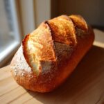 A freshly baked, golden brown loaf of homemade french bread resting on a wooden cutting board.