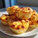 A stack of golden brown, high-protein egg bites topped with crispy bacon pieces, served on a white plate.