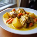 A close-up serving of rich, yellow Jamaican curry chicken stewed with large chunks of potato and carrots.