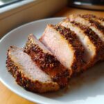 Close-up of several thick slices of perfectly cooked pork loin roast with a dark, seasoned crust.