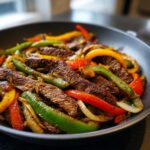 Close-up of perfectly cooked steak fajitas with colorful bell peppers and onions in a dark skillet.