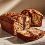 Close-up of moist apple bread loaf with a slice cut, showing visible apple chunks and a brown cinnamon swirl.