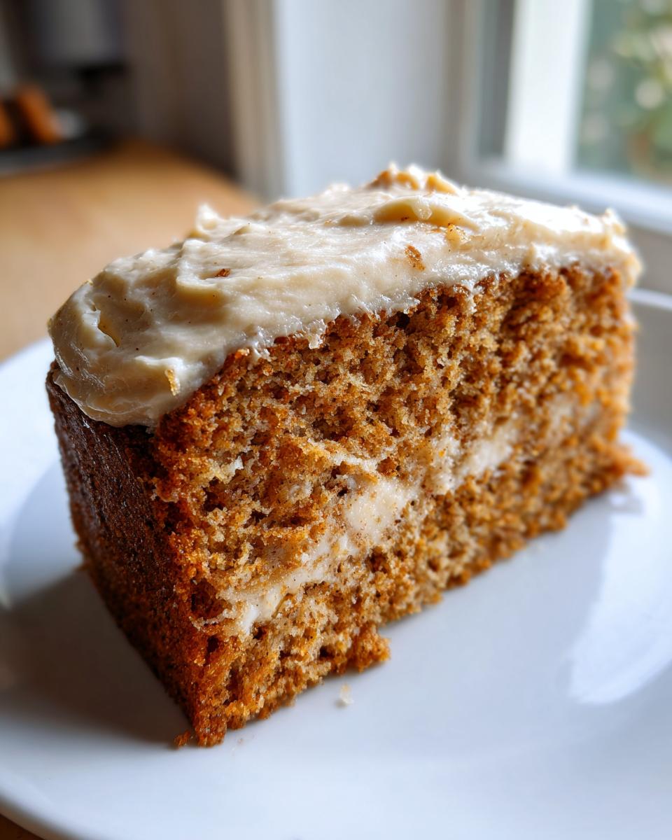 Close-up of a thick slice of moist applesauce cake with a layer of cream cheese frosting on top and in the middle.